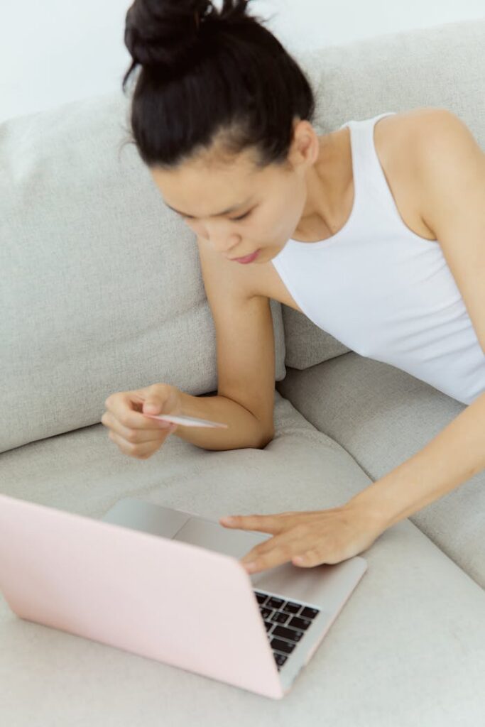 Woman lying on a sofa using laptop and credit card for online shopping.